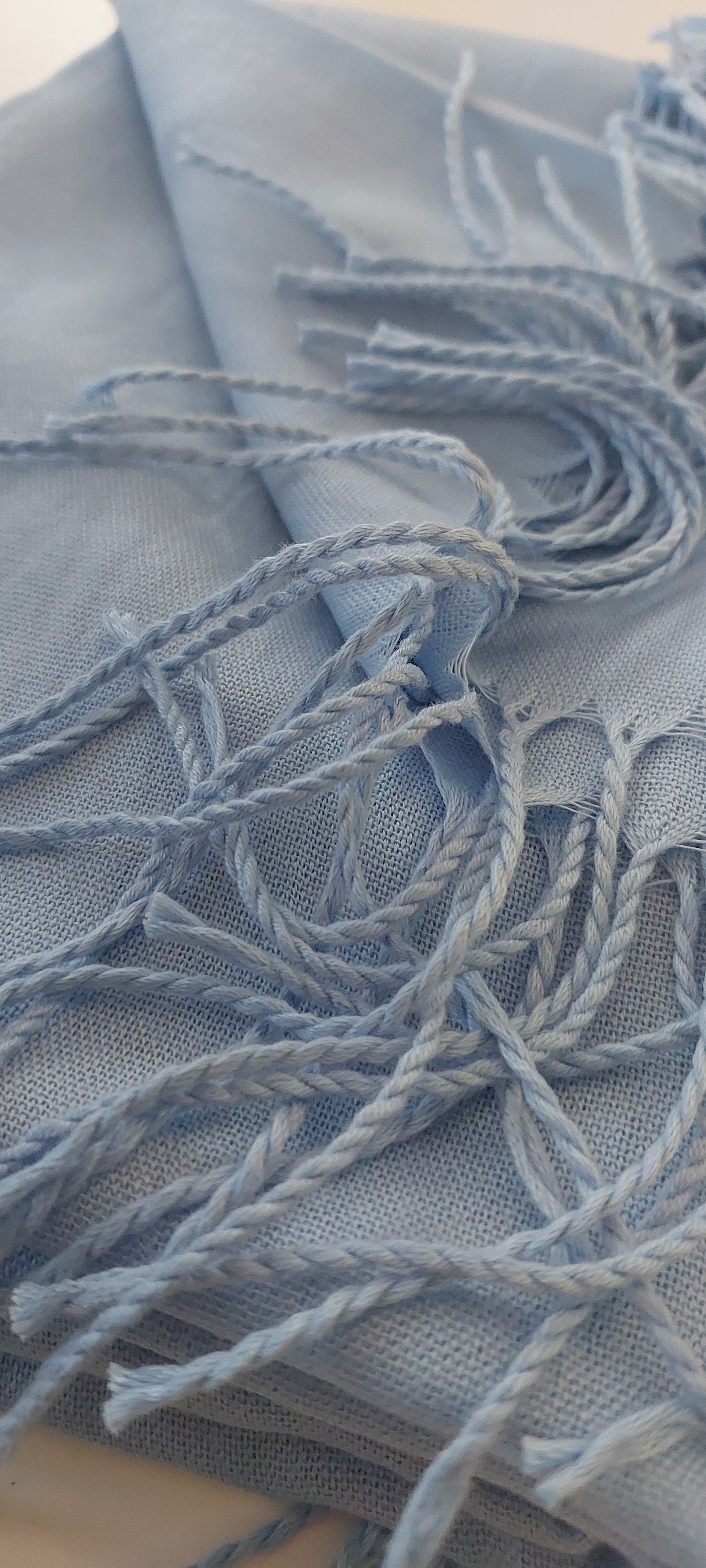 Close-up of baby blue scarf with tassels on white background