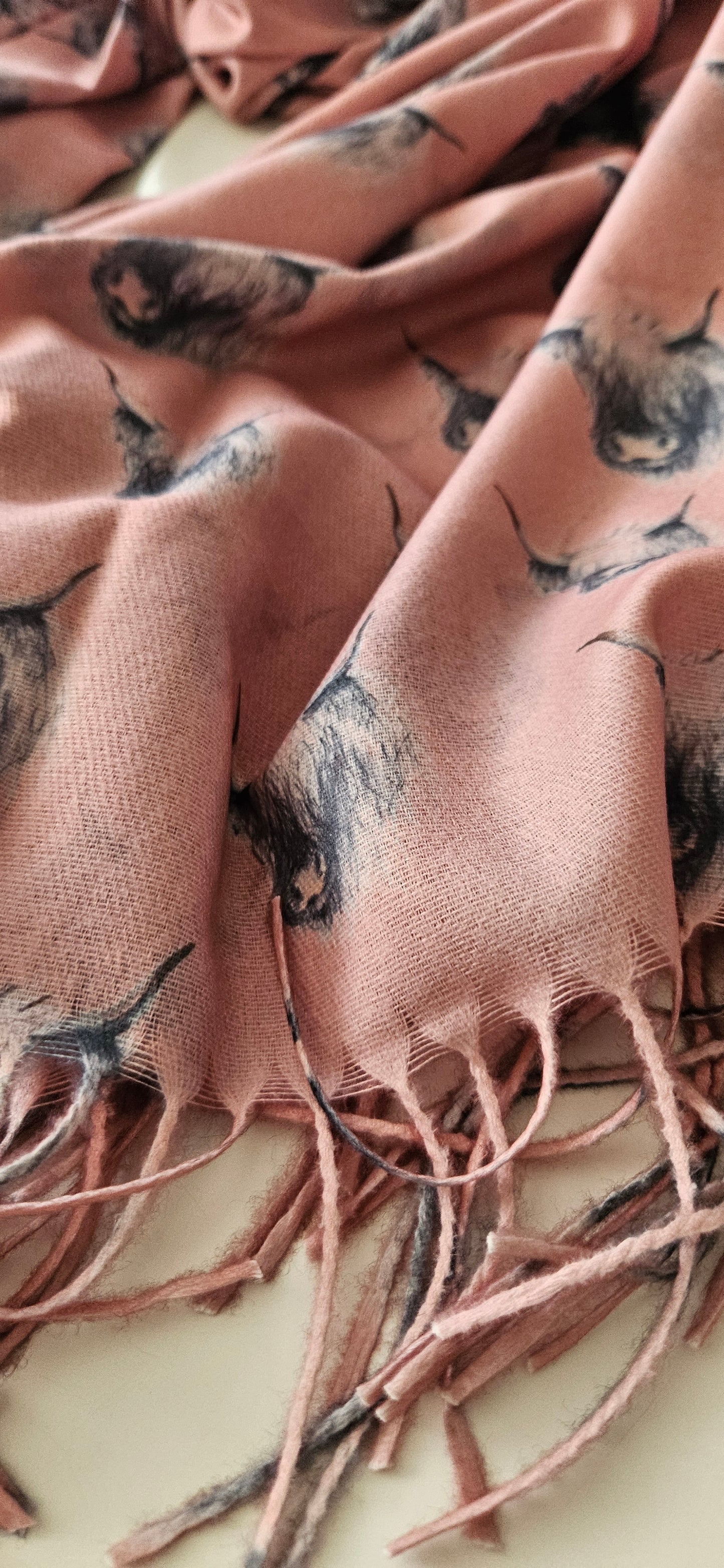 Close-up of a pink scarf with black & white highland cow pattern and tassels.