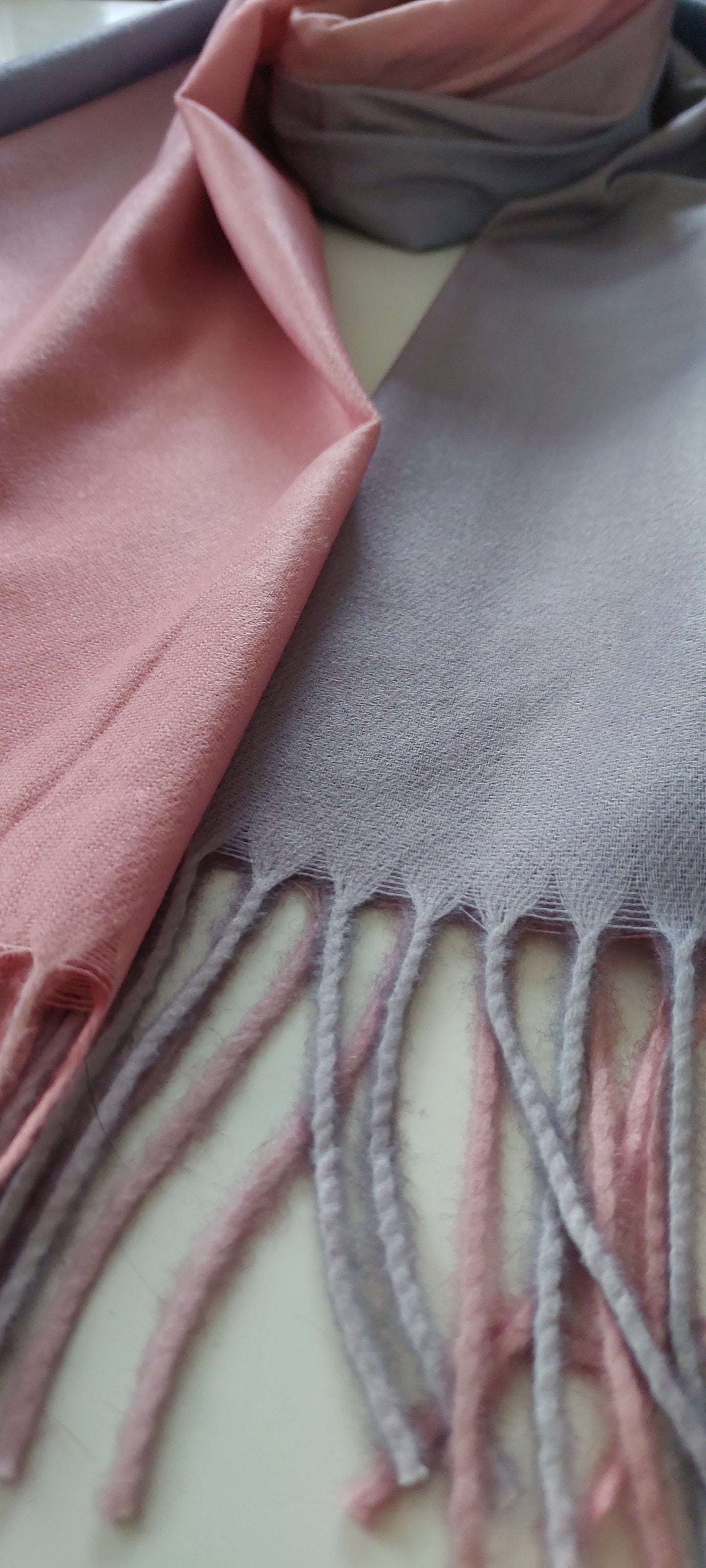 Close-up of a pink and lilac scarf with fringed edge on a plain background