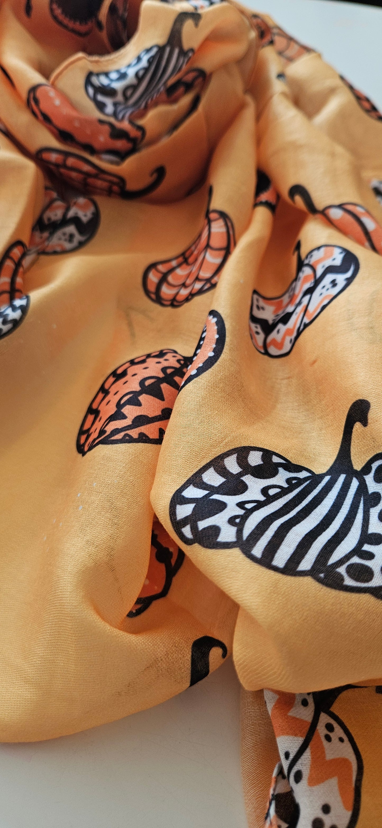 Close Up image of Orange scarf with black, white and Orange pumpkins on, laid flat on a white background
