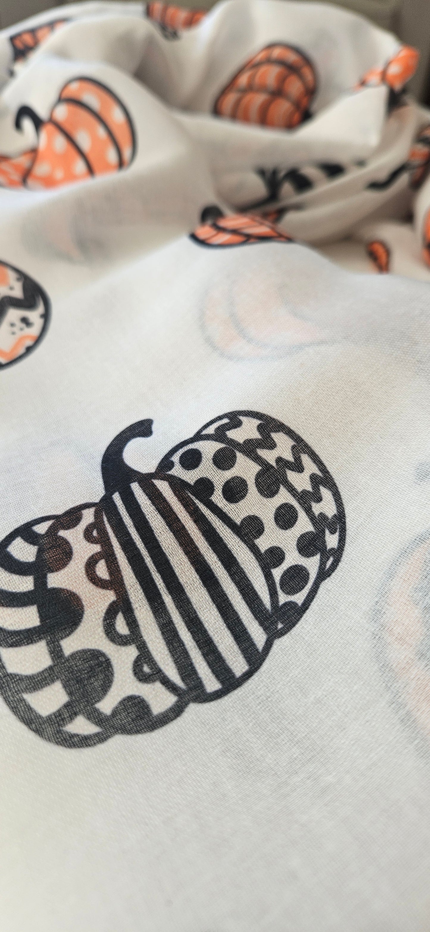 Close-up of a white scarf with black and orange pumpkin patterned design