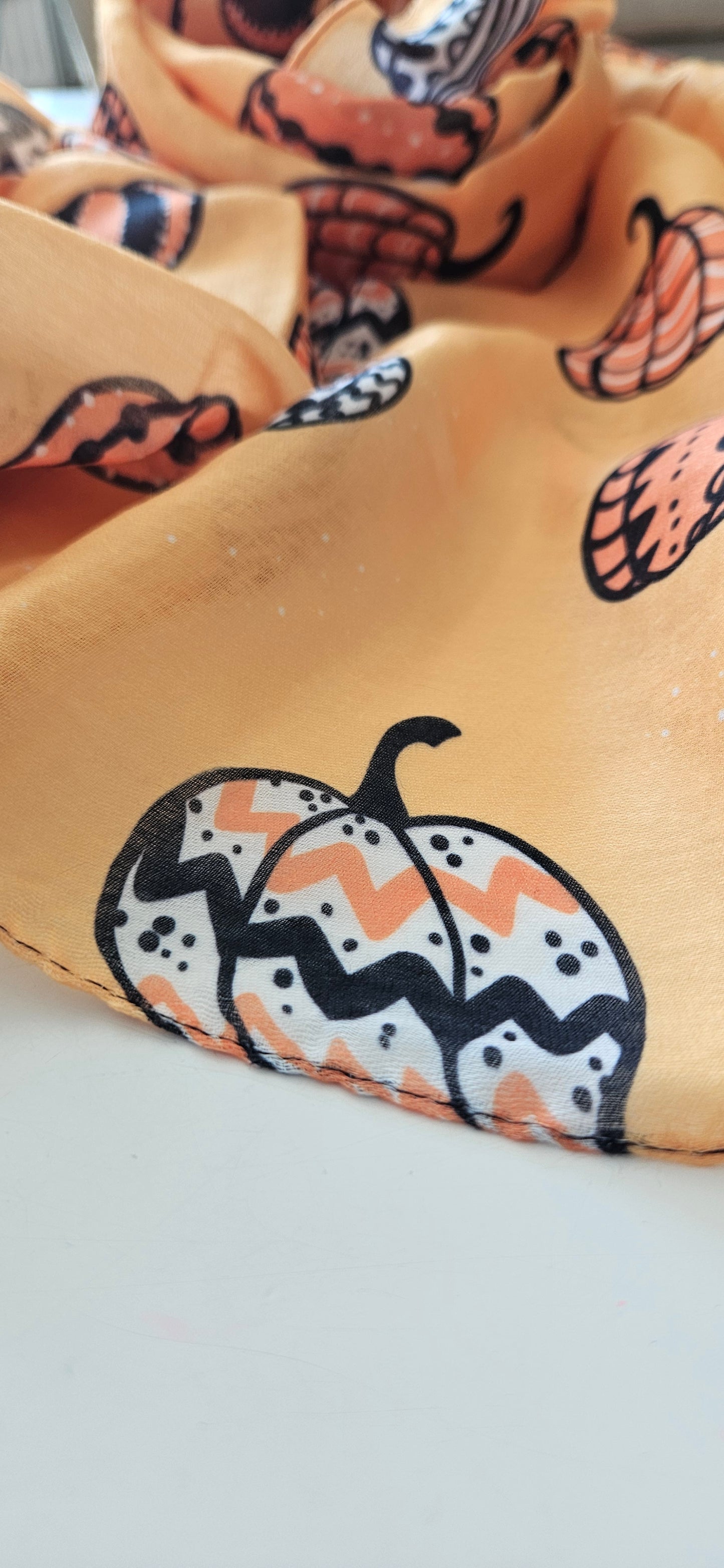 Close-up of a orange scarf with black and orange pumpkin patterns on a white background