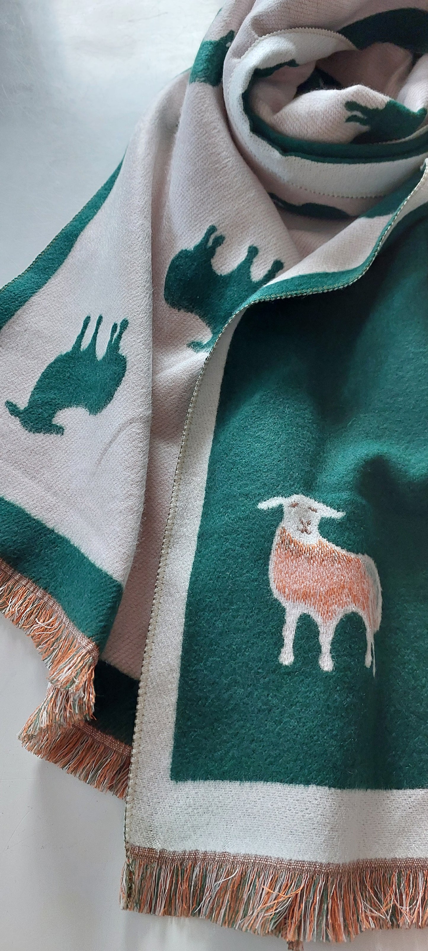 Green scarf with sheep patterns and fringe on a white background