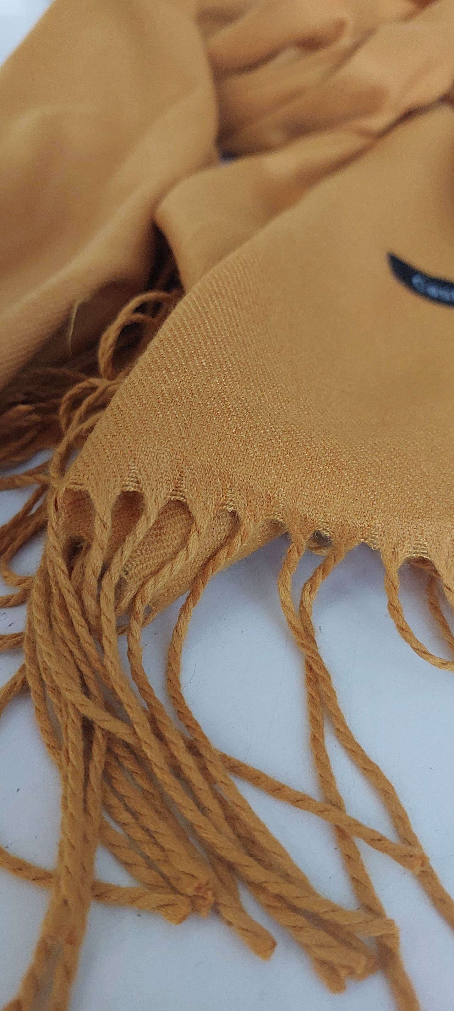 Close-up of a mustard pashmina with fringes on a white background