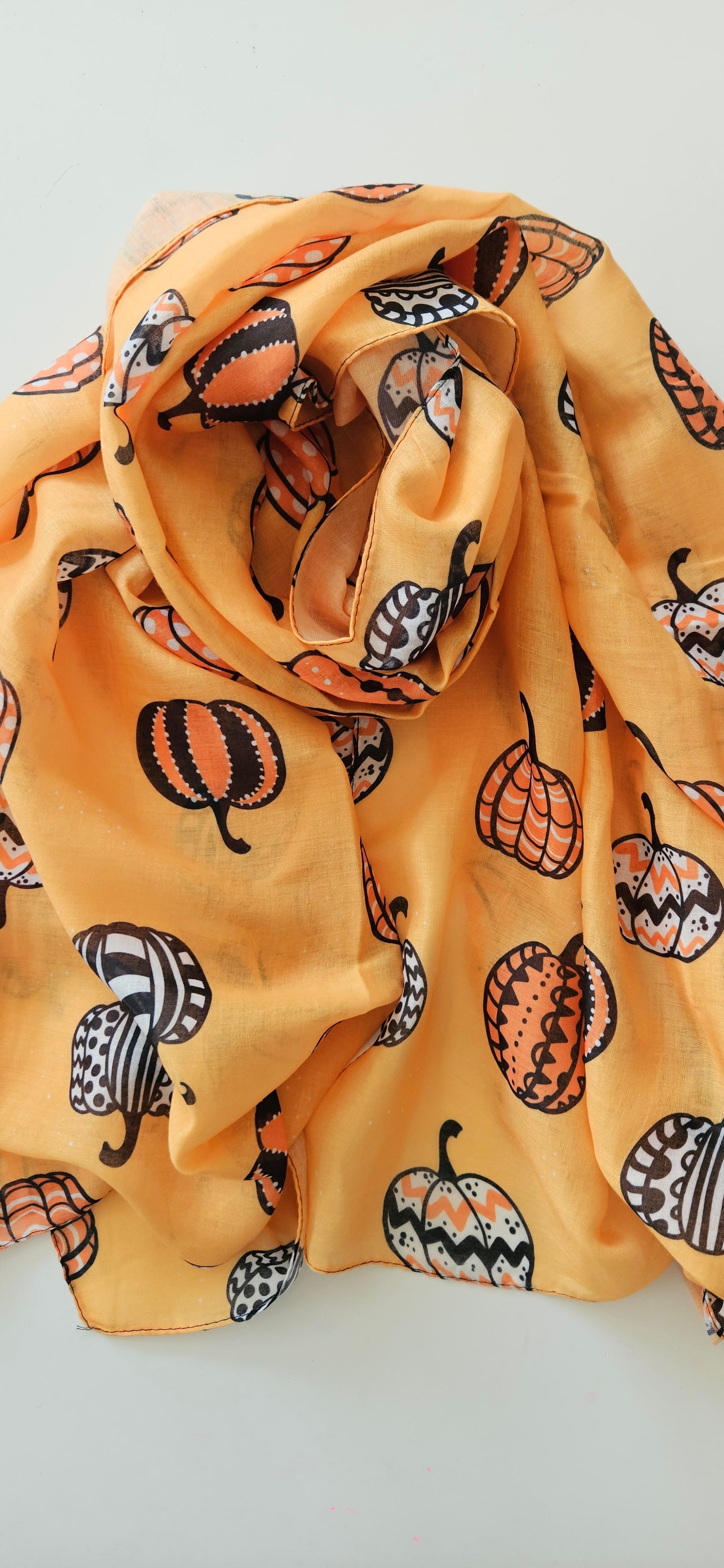 Orange scarf fabric with White Black and Orange patterned pumpkins on it, laid flat on a white background