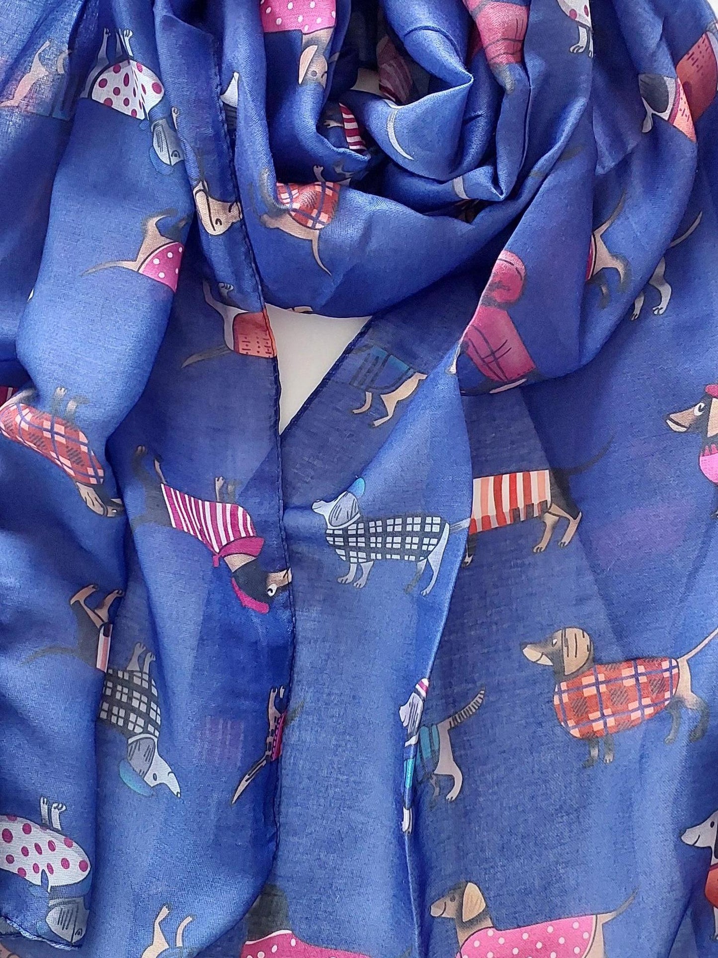 Rolled-up blue scarf with sausage dogs in jackets on a white background