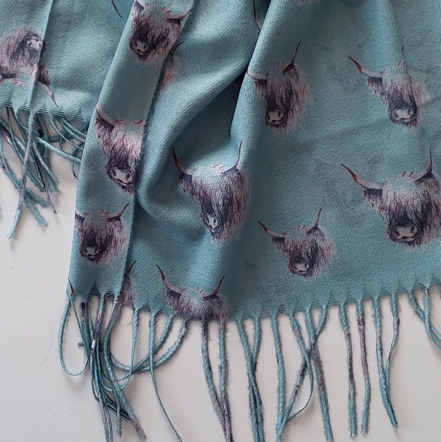Sage scarf with highland cow pattern and fringes on a white background