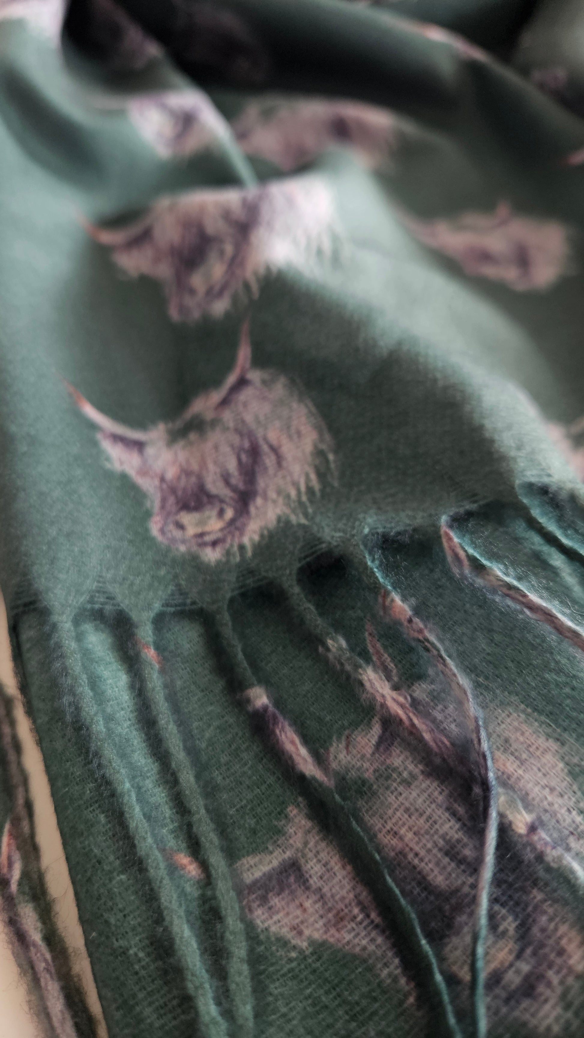 Close up of bottle green coloured pashmina with Monochromatic Highland cow heads on, with Tassels