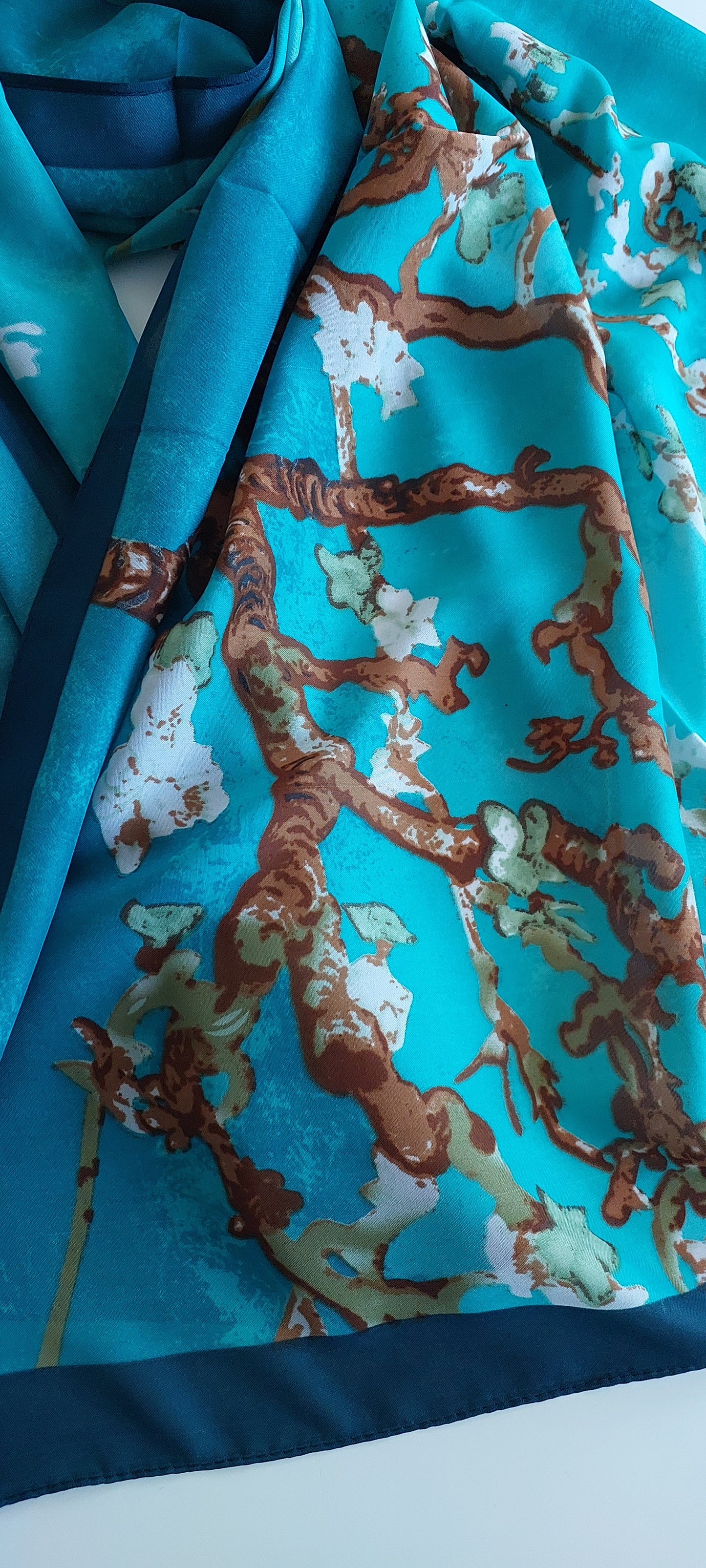 Close-up of a teal scarf with a floral pattern on a white background