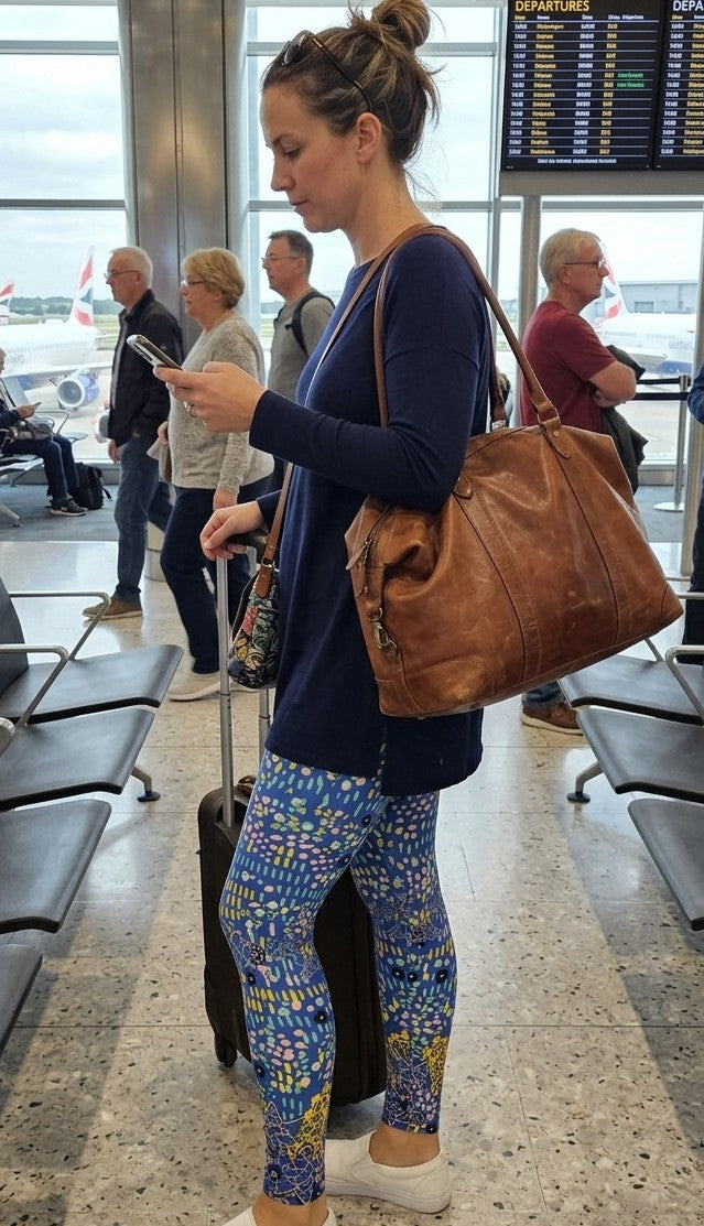 Woman in an airport wearing colourful leggings and a brown bag, looking at her phone.