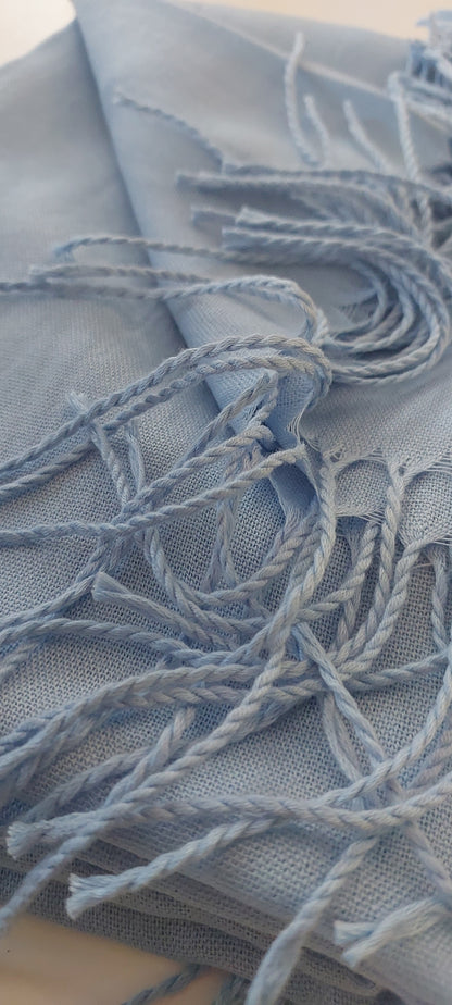 Close-up of baby blue scarf with tassels on white background