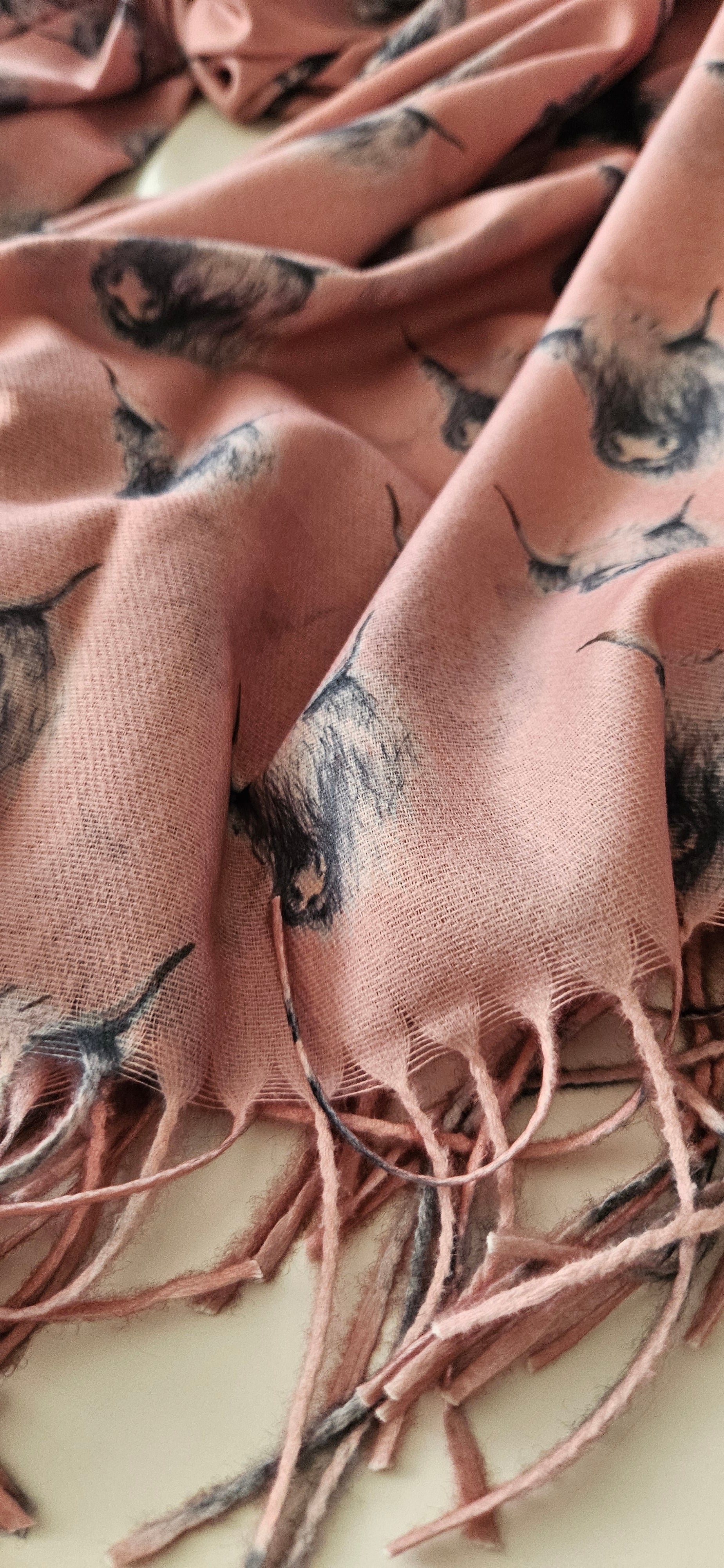 Close-up of a pink scarf with black & white highland cow pattern and tassels.