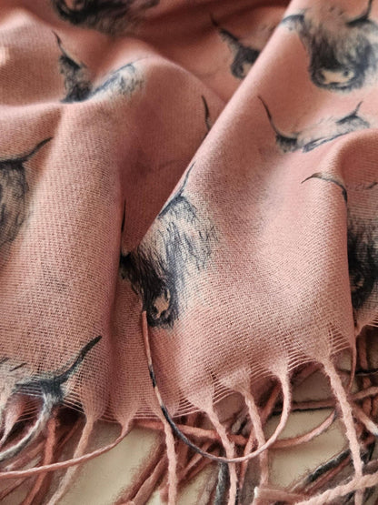 Close-up of a pink scarf with black & white highland cow pattern and tassels.
