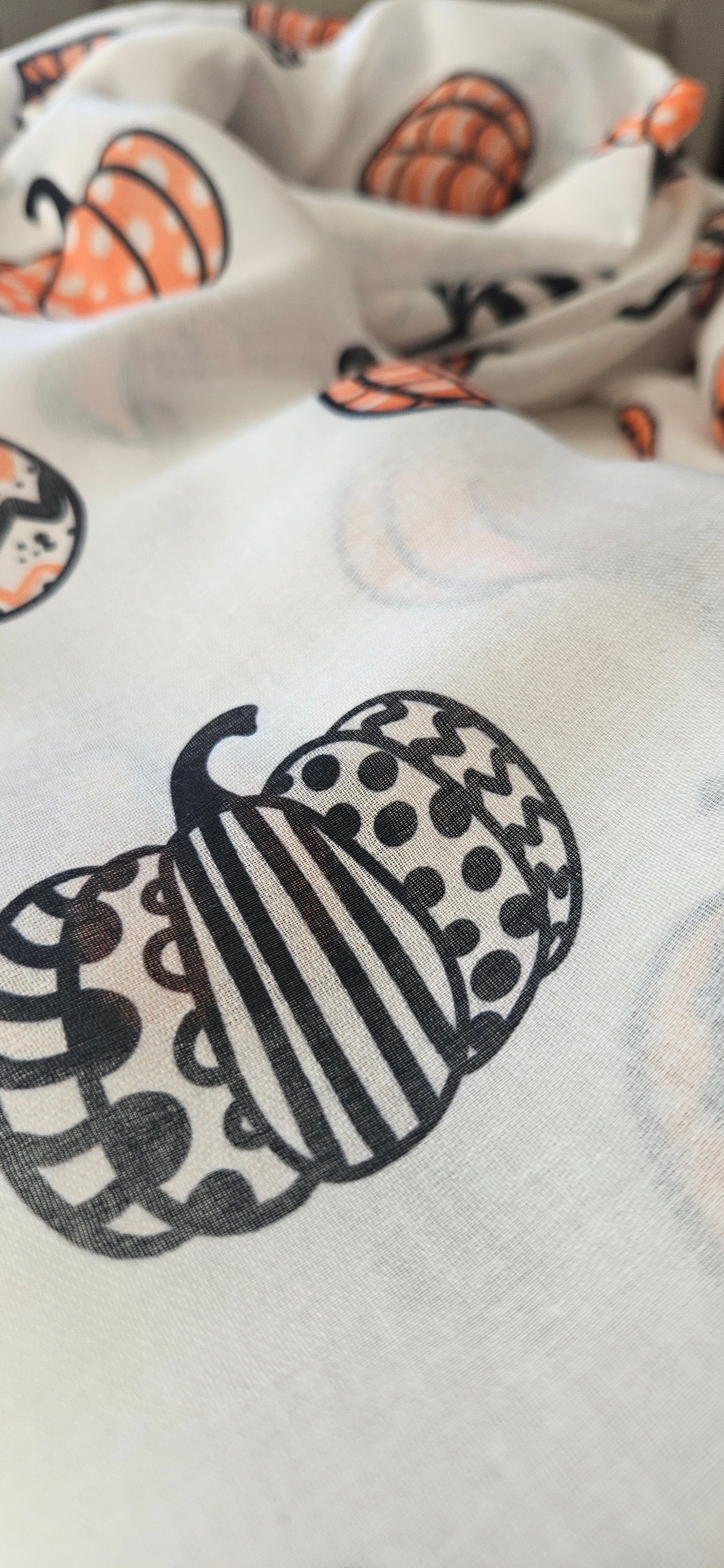 Close-up of a white scarf with black and orange pumpkin patterned design