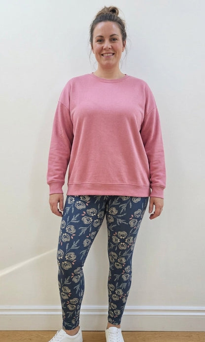Person wearing a pink sweatshirt and blue floral leggings against a white wall.