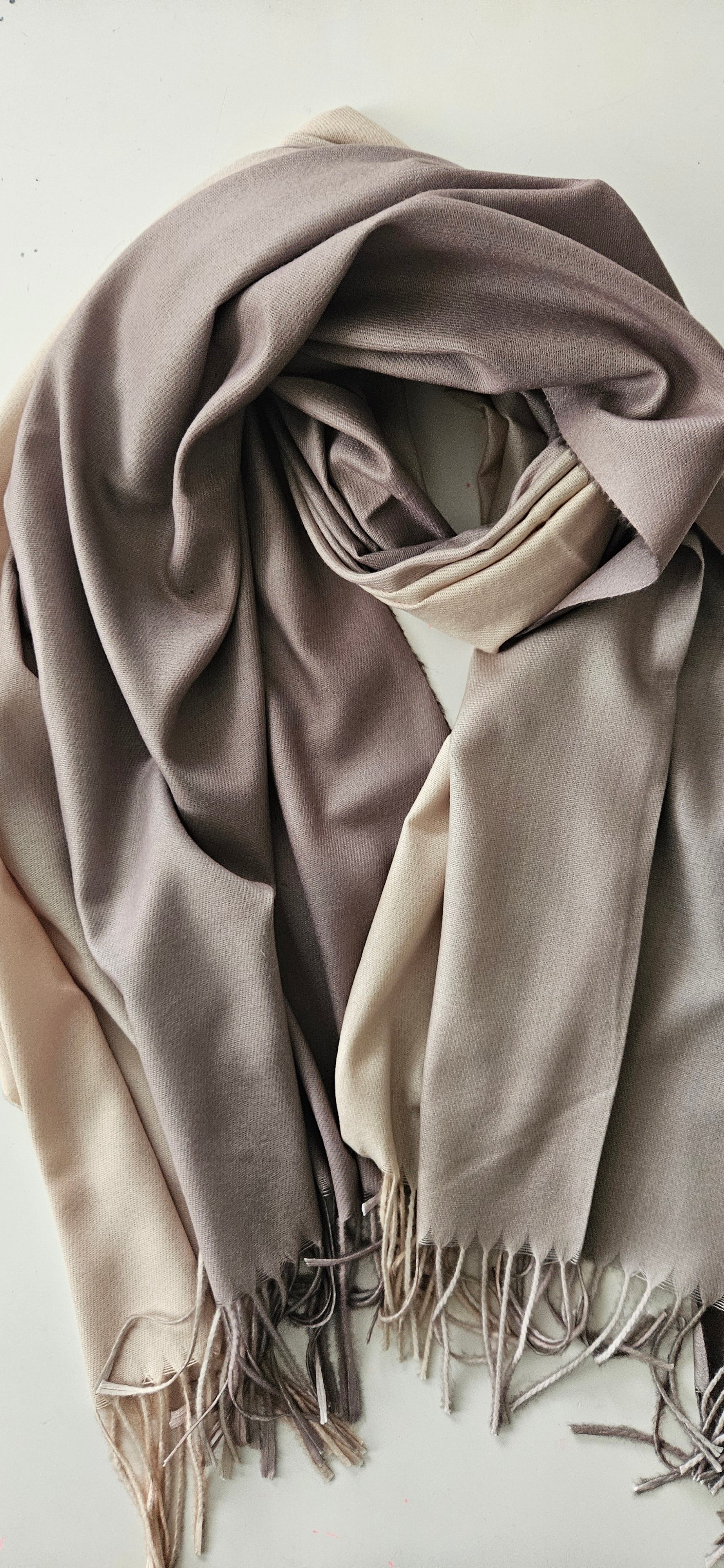 Folded beige and brown scarf with tassels on a light background