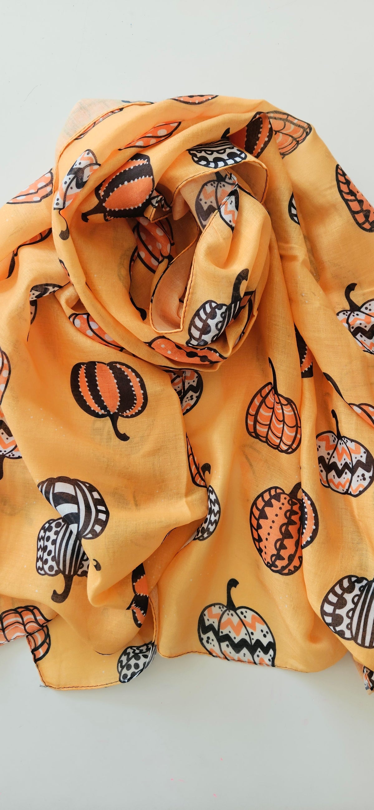 Orange scarf fabric with White Black and Orange patterned pumpkins on it, laid flat on a white background
