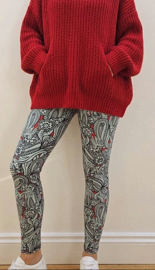 Person wearing a red sweater and patterned leggings against a white wall.