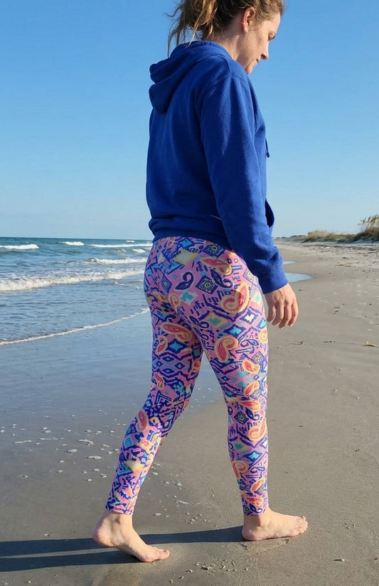 Person wearing colorful patterned leggings and a blue hoodie on a beach.