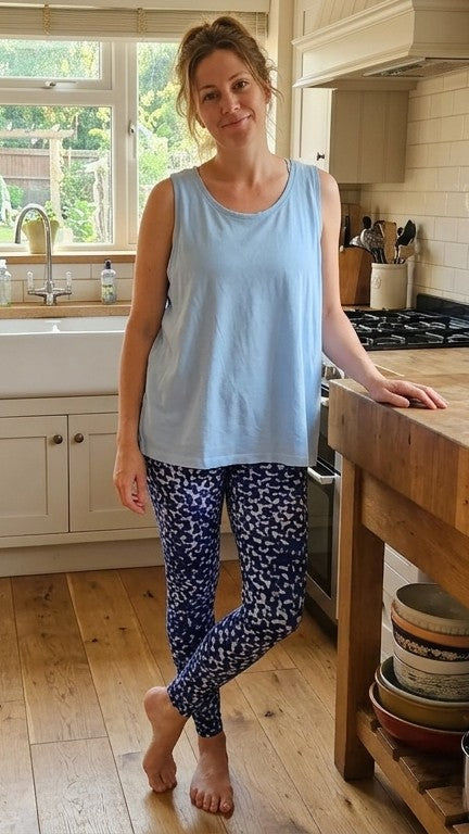 Woman standing in a kitchen wearing a light blue tank top and patterned Shimena leggings.