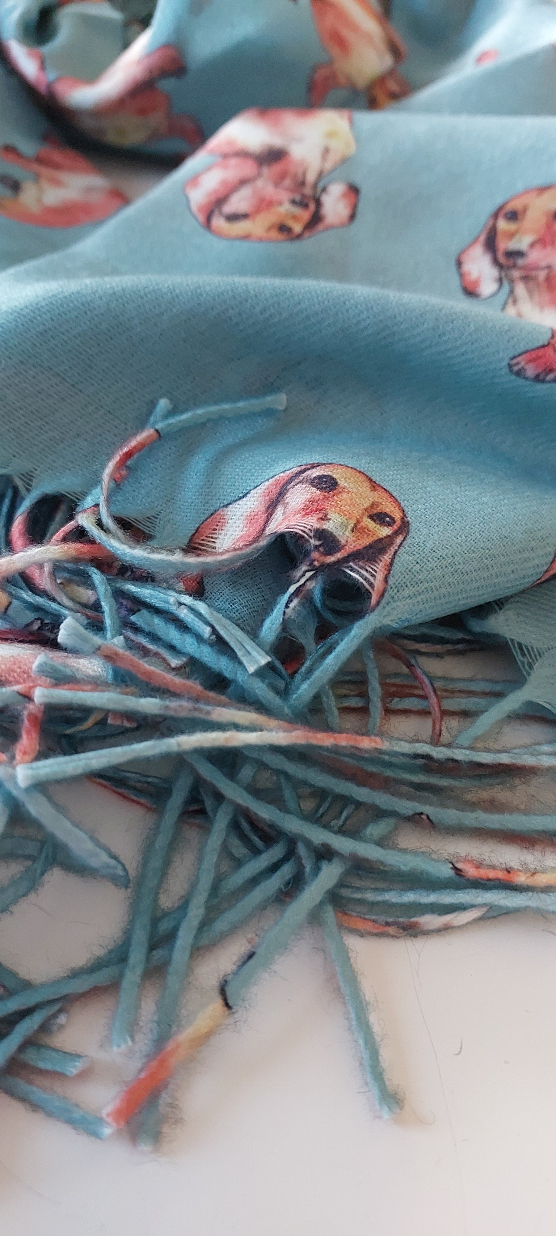 Close-up of a pashmina with dachshund pattern and turquoise tassels on a white background